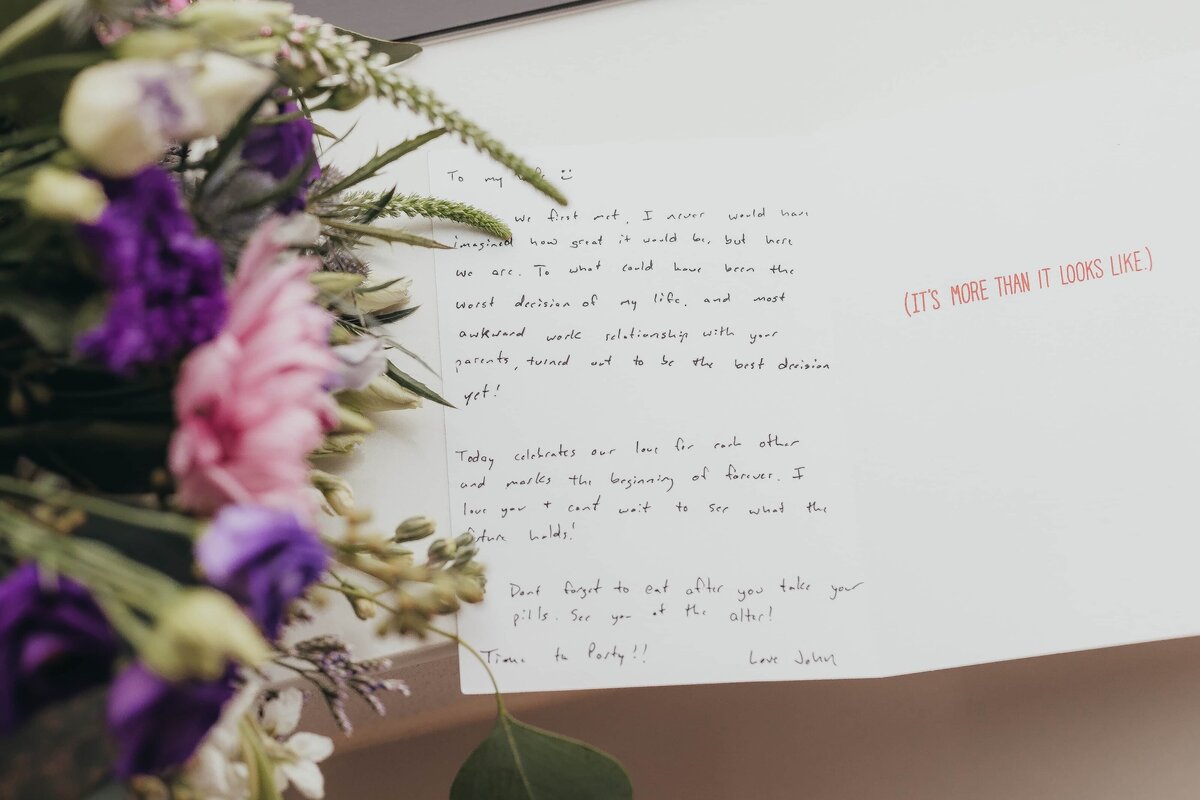A handwritten letter on white paper accompanied by a bouquet of purple and green flowers, with text partially visible, possibly from an Iowa wedding.