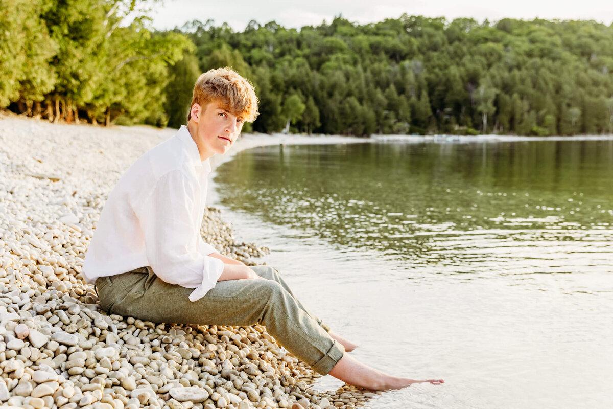 high school senior boy sitting on a beach captured by Door County Photographer Ashley Kalbus
