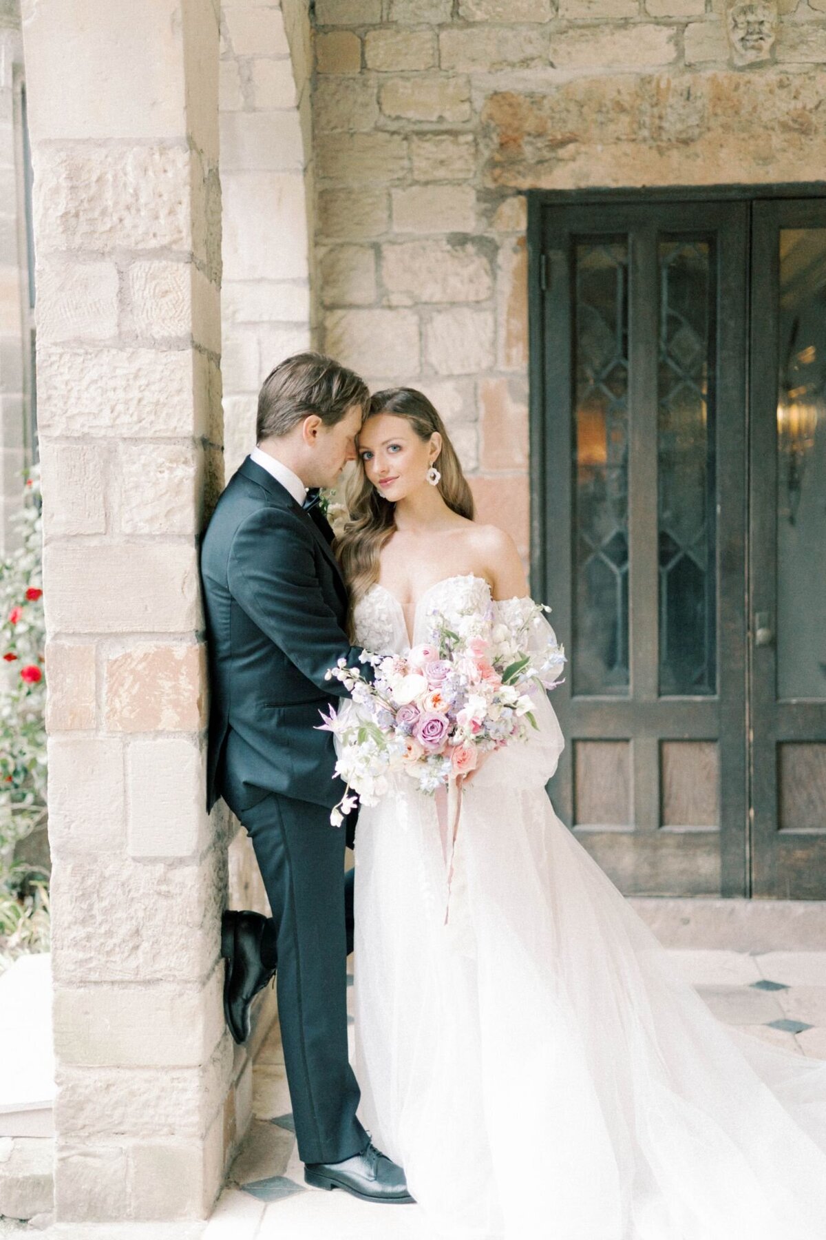 Bride and groom embrace romantically against stone post.