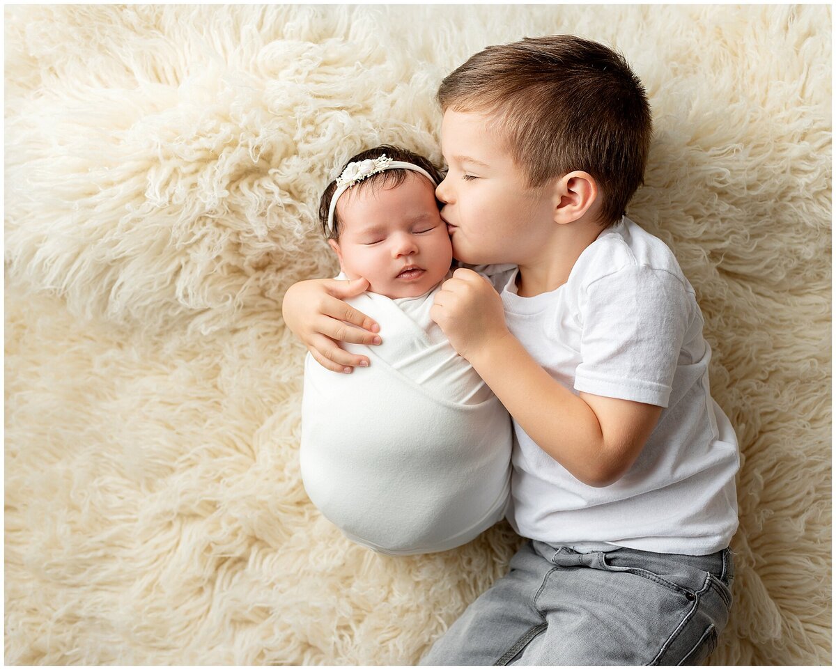 brother kissing newborn sister on cheek