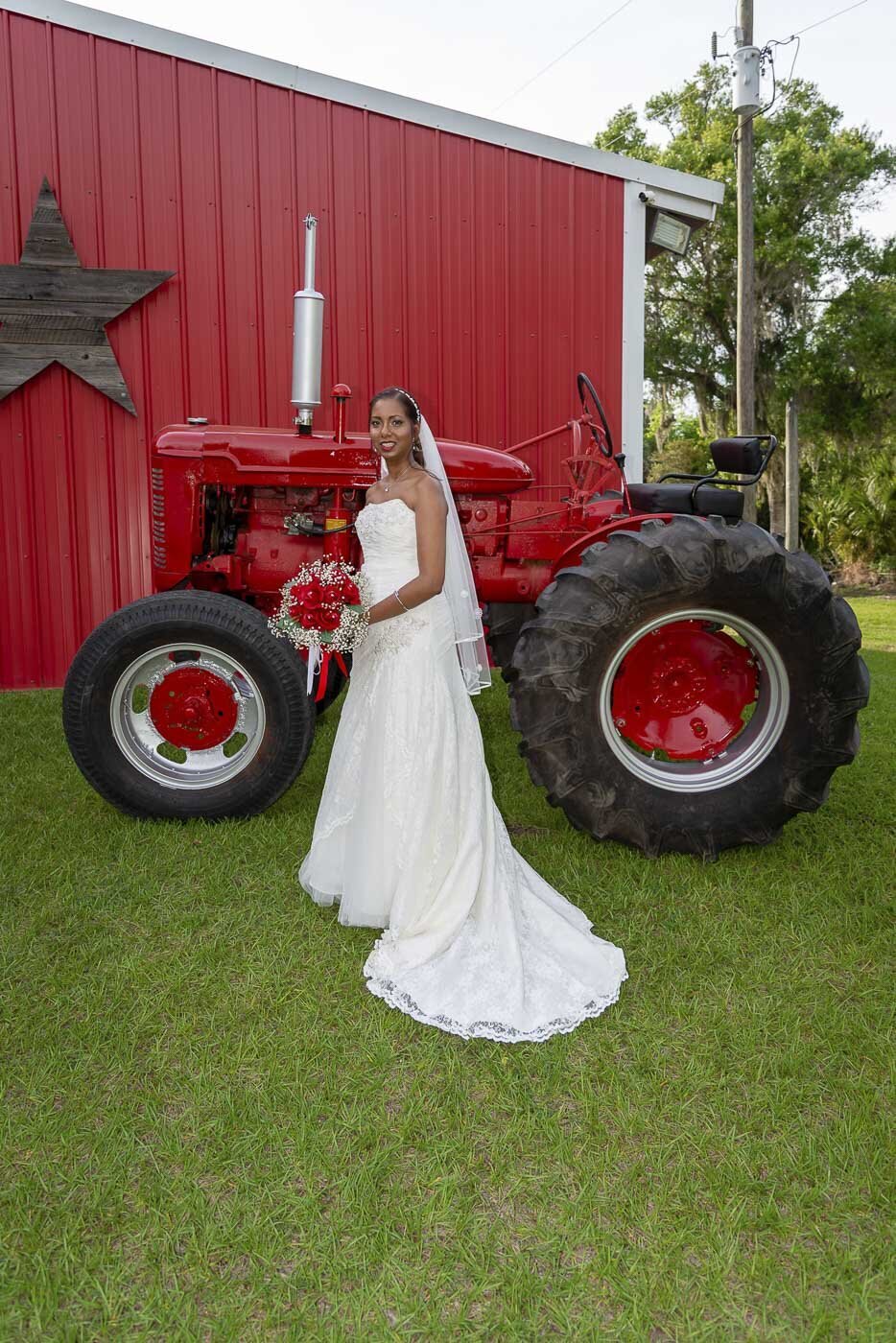 A bride poses in front of a red tractor and a red barn.
