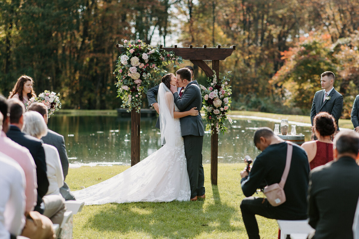 bride and groom's first kiss with guests sitting down on either side of the aisle