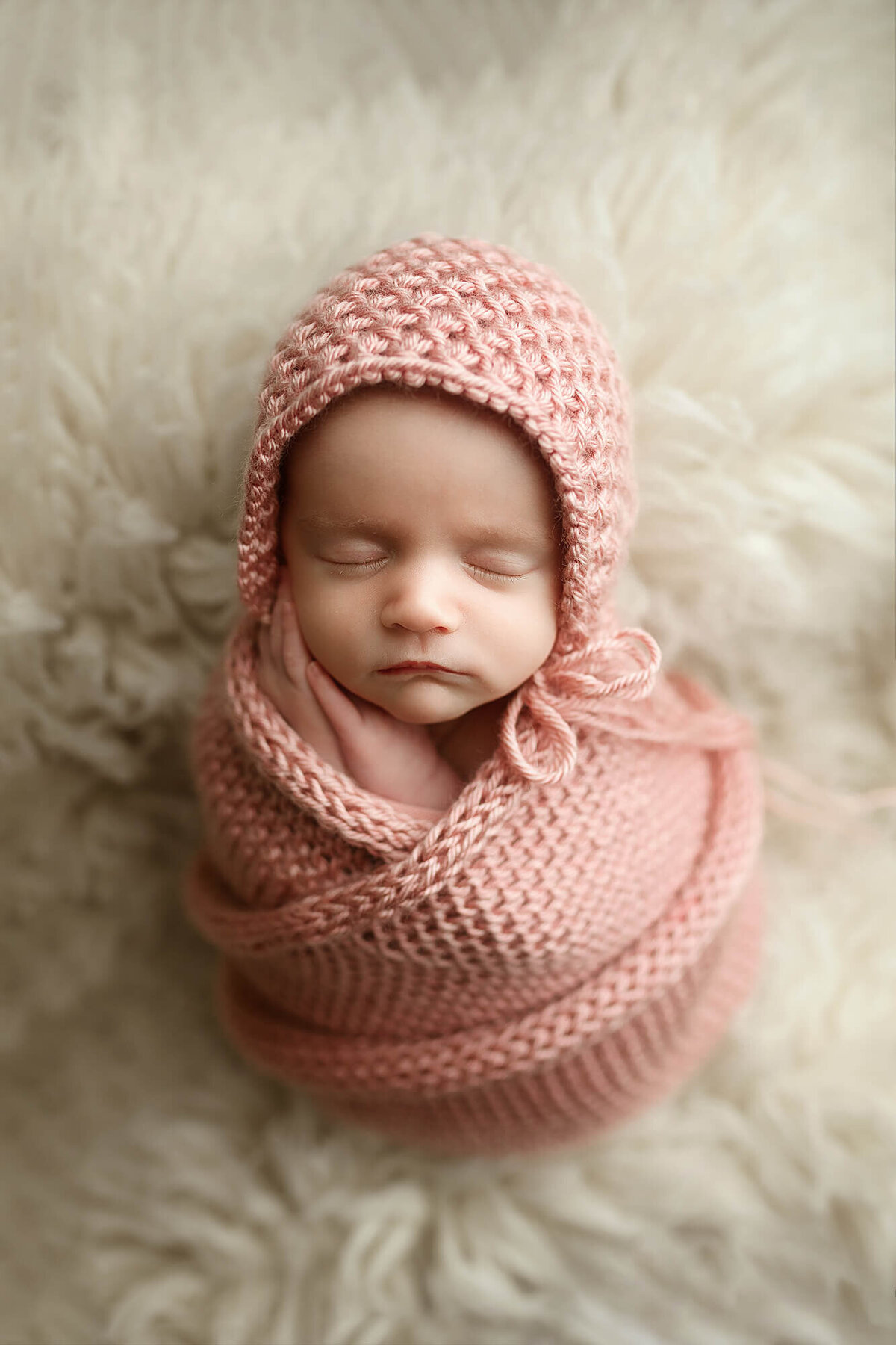 Baby girl wrapped in a pink knitted blanket with matching bonnet.