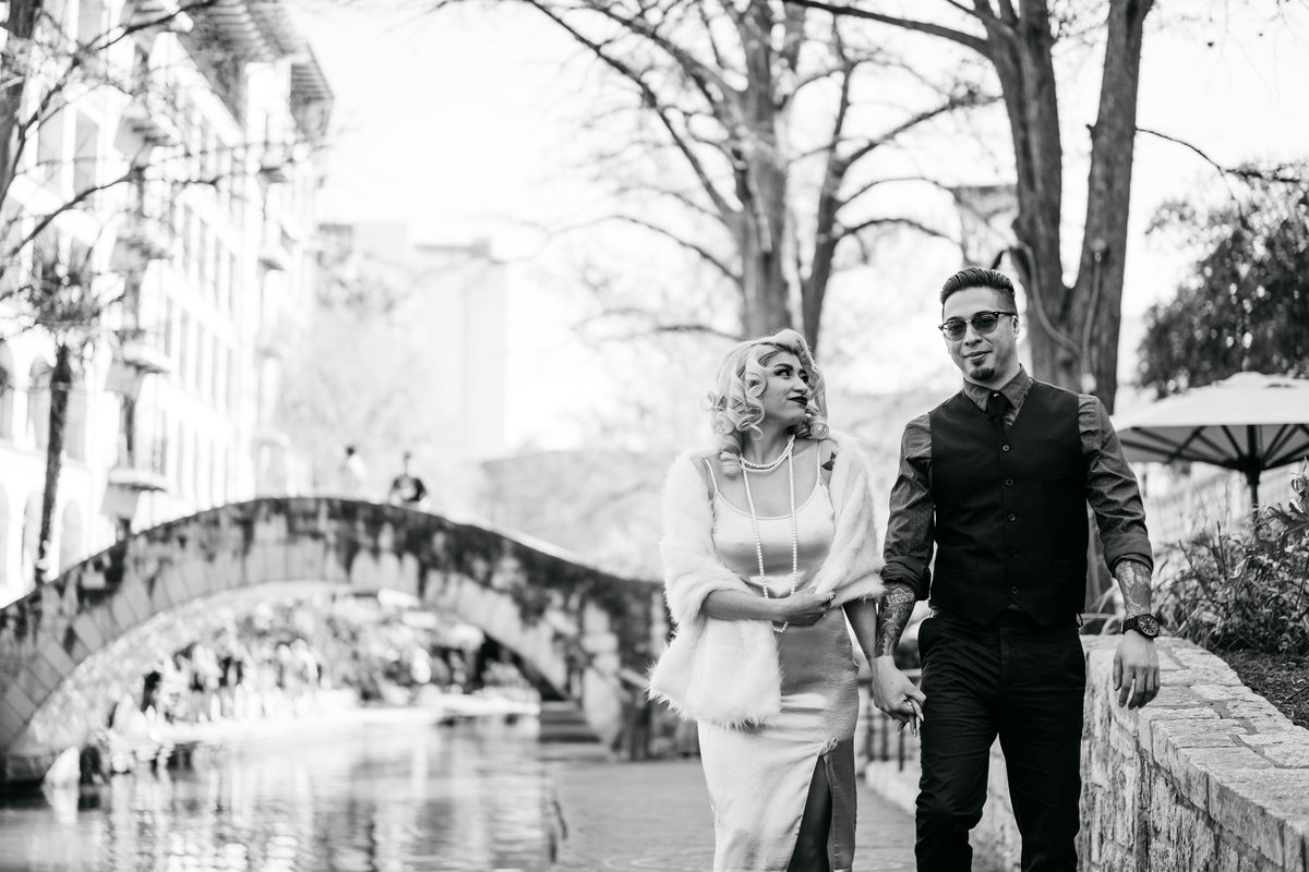Black and white picture of engaged couple walking on the banks of the San Antonio River Walk downtown.
