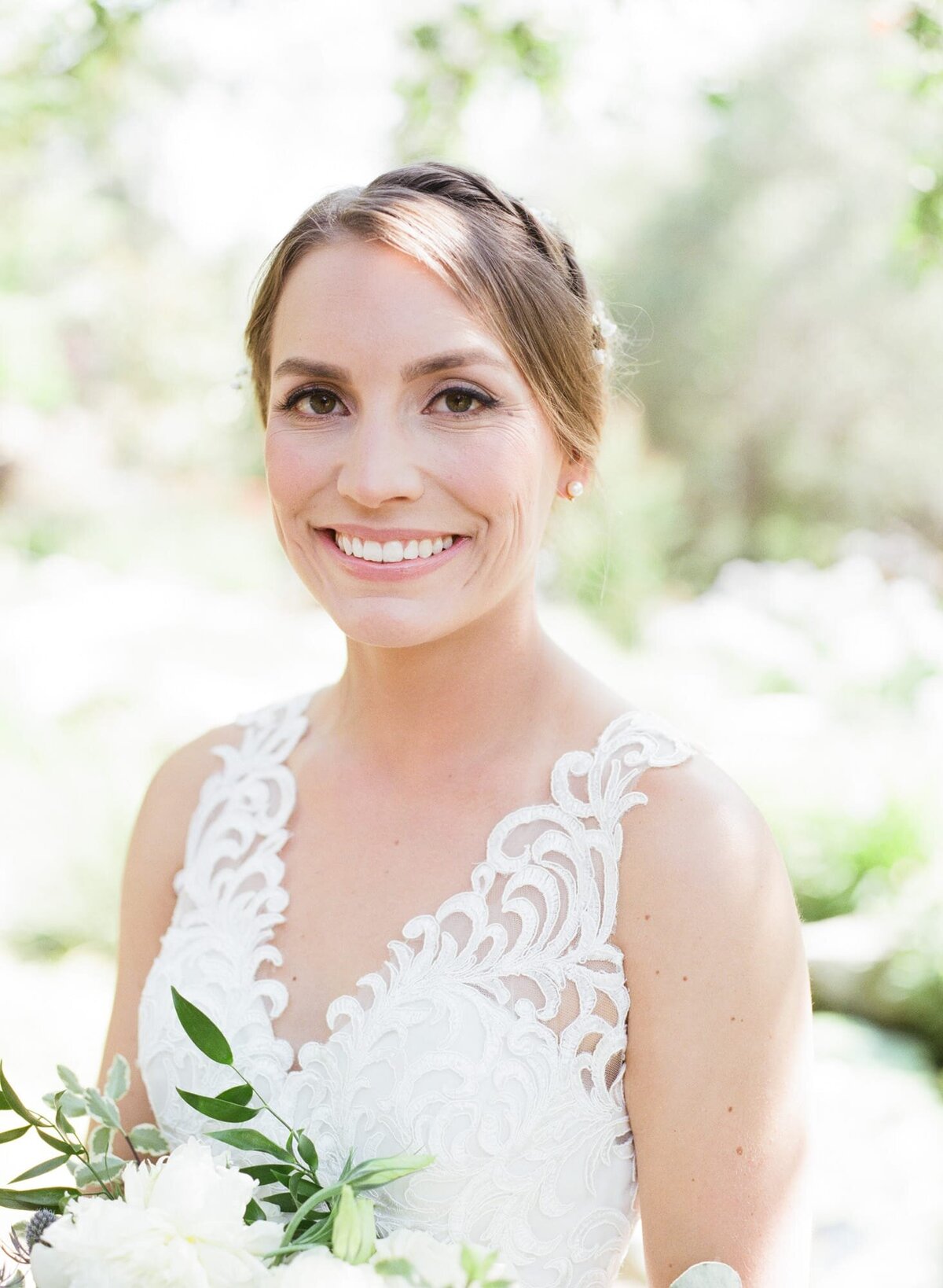 Bride poses with a bouquet of white flowers while wearing a sleeveless wedding dress.