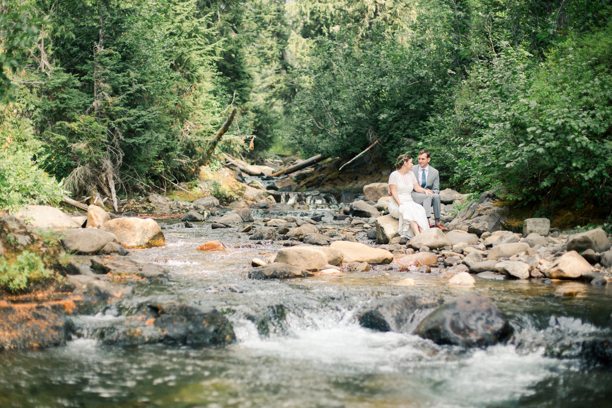 couple sits on rocks of river in mount rainier national forest