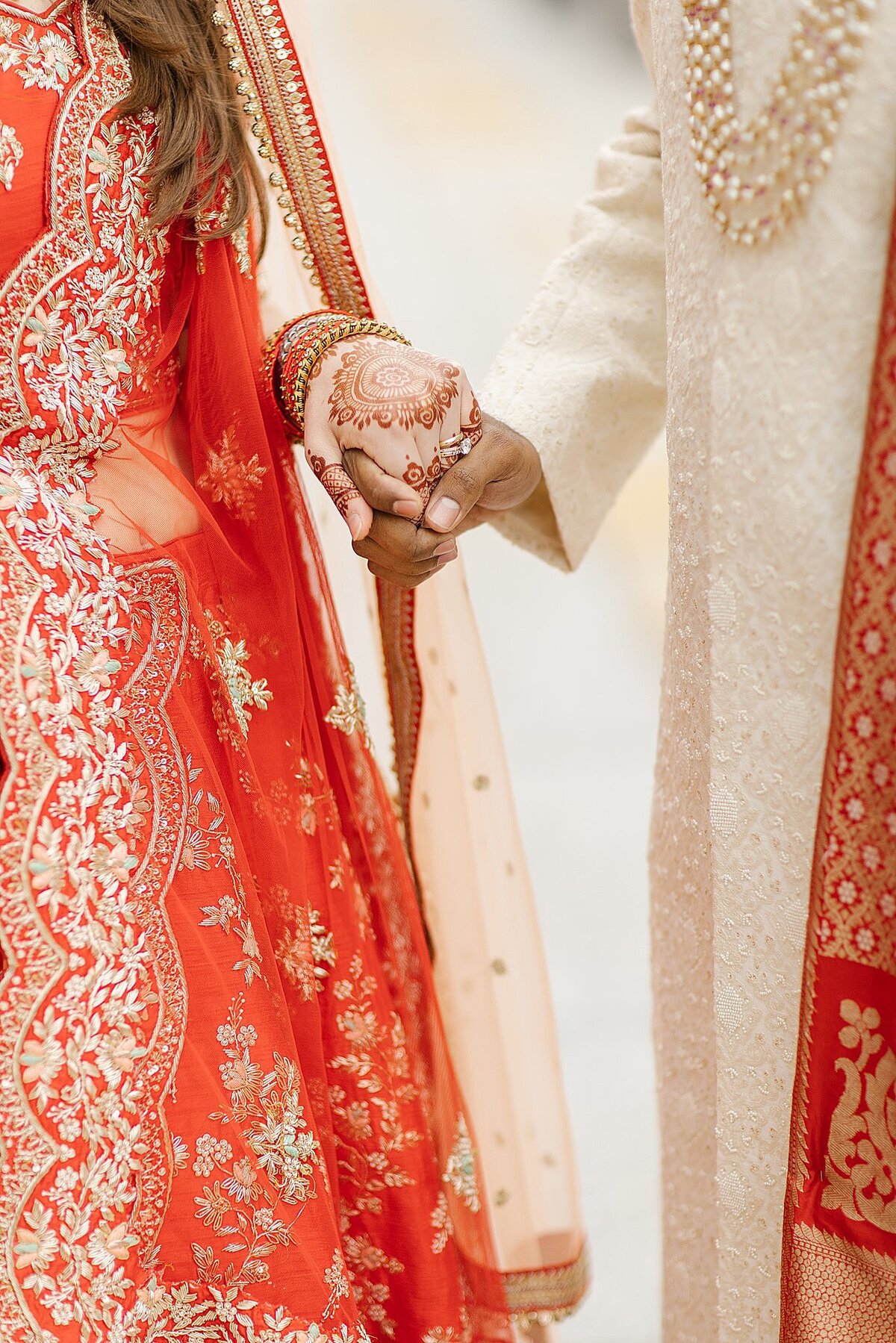 Hindu bride dressed in a red and gold saree and Indian groom dressed in a white and red sherwani hold hands at their Indian Wedding in Nashville, TN