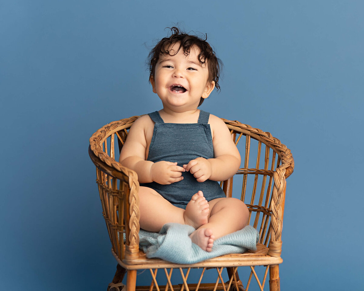 baby boy laughing with his feet up on chair in pdx photography studio for first birthday