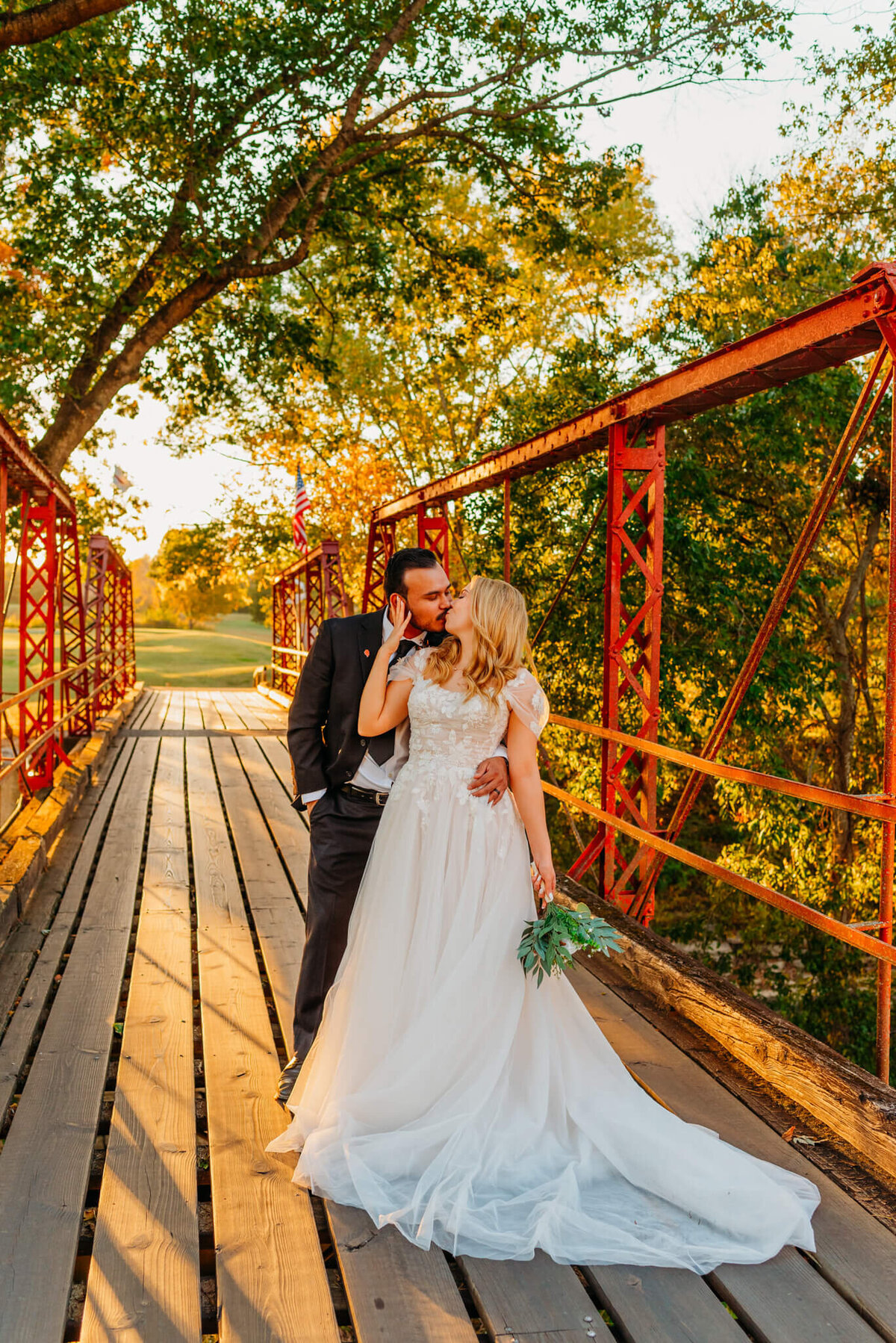 photo of a groom hugging the bride from behind while standing on a wooden bridge