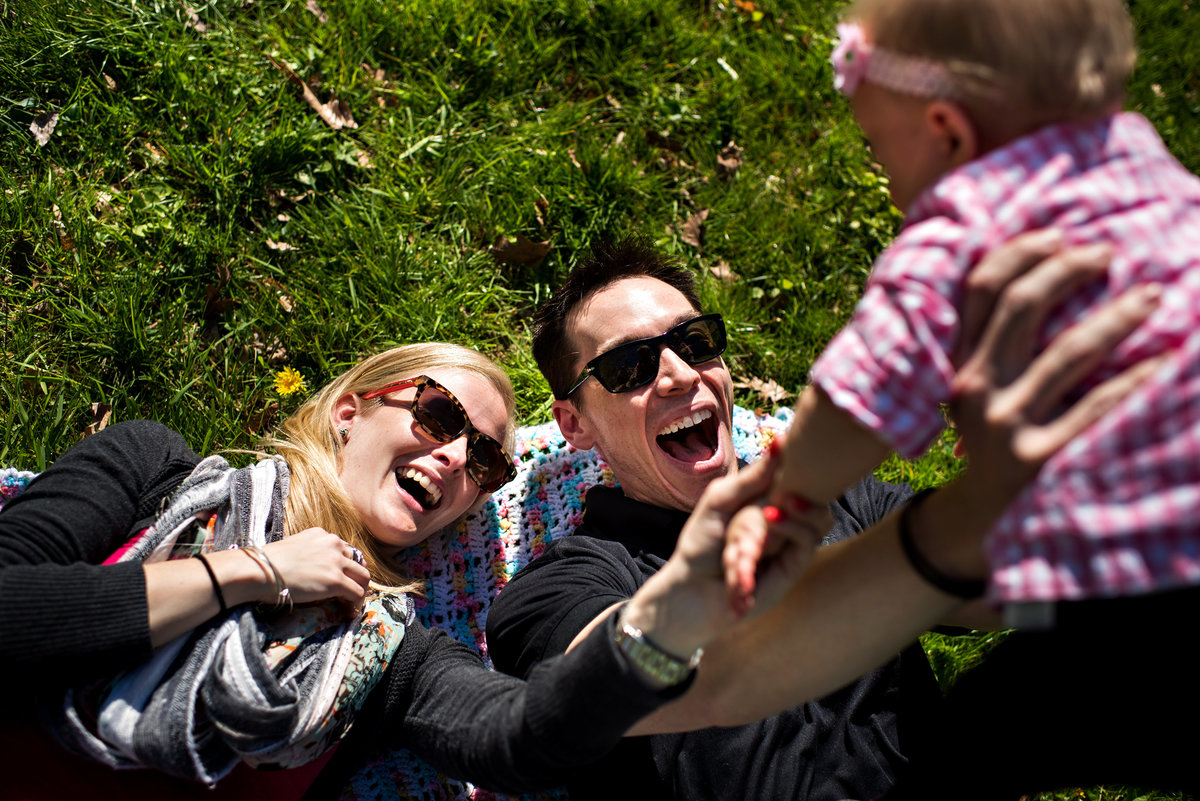 New parents lay on the grass in the park and lift their baby over their heads.