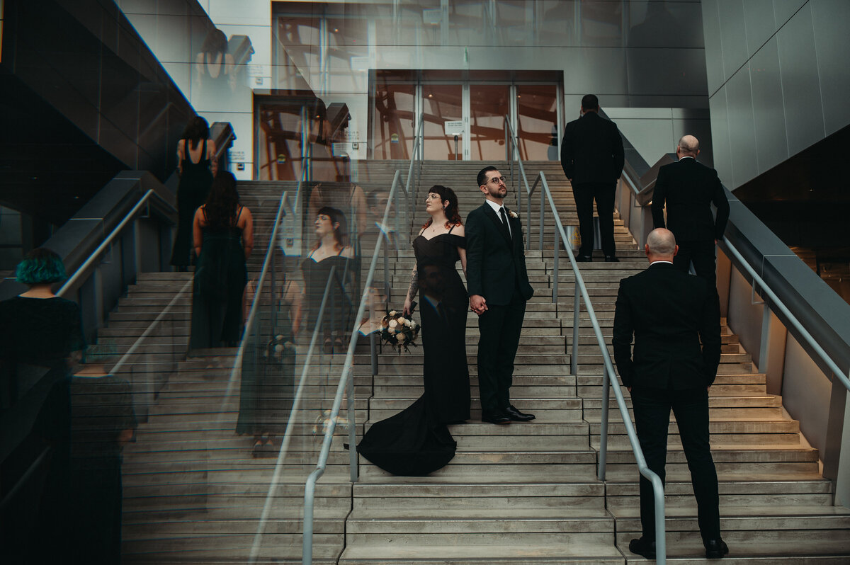 Couple stands on Akron Museum stairs with their wedding party for a unique and serious pose.
