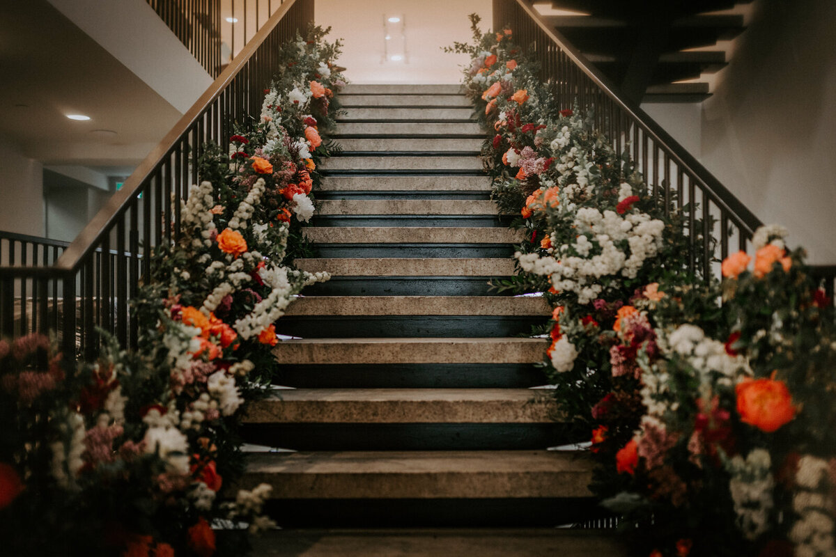 Beautiful staircase lined with florals at The Pioneer, a historical industrial wedding venue in Calgary, featured on the Brontë Bride Vendor Guide.