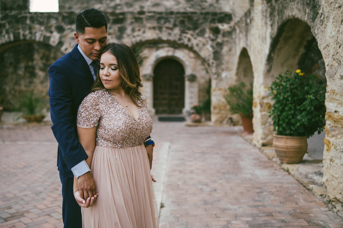 Gorgeous engaged hispanic couple standing by the arches at Mission San Jose in San Antonio.