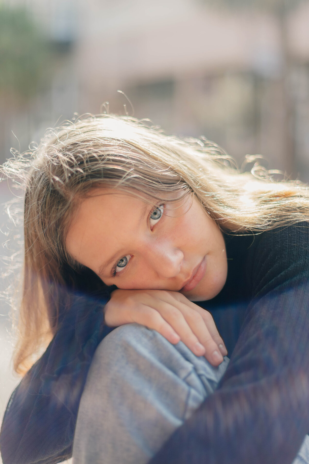 A lens flare surrounds a senior girl while her head rests on her hand on her knee while looking into the camera