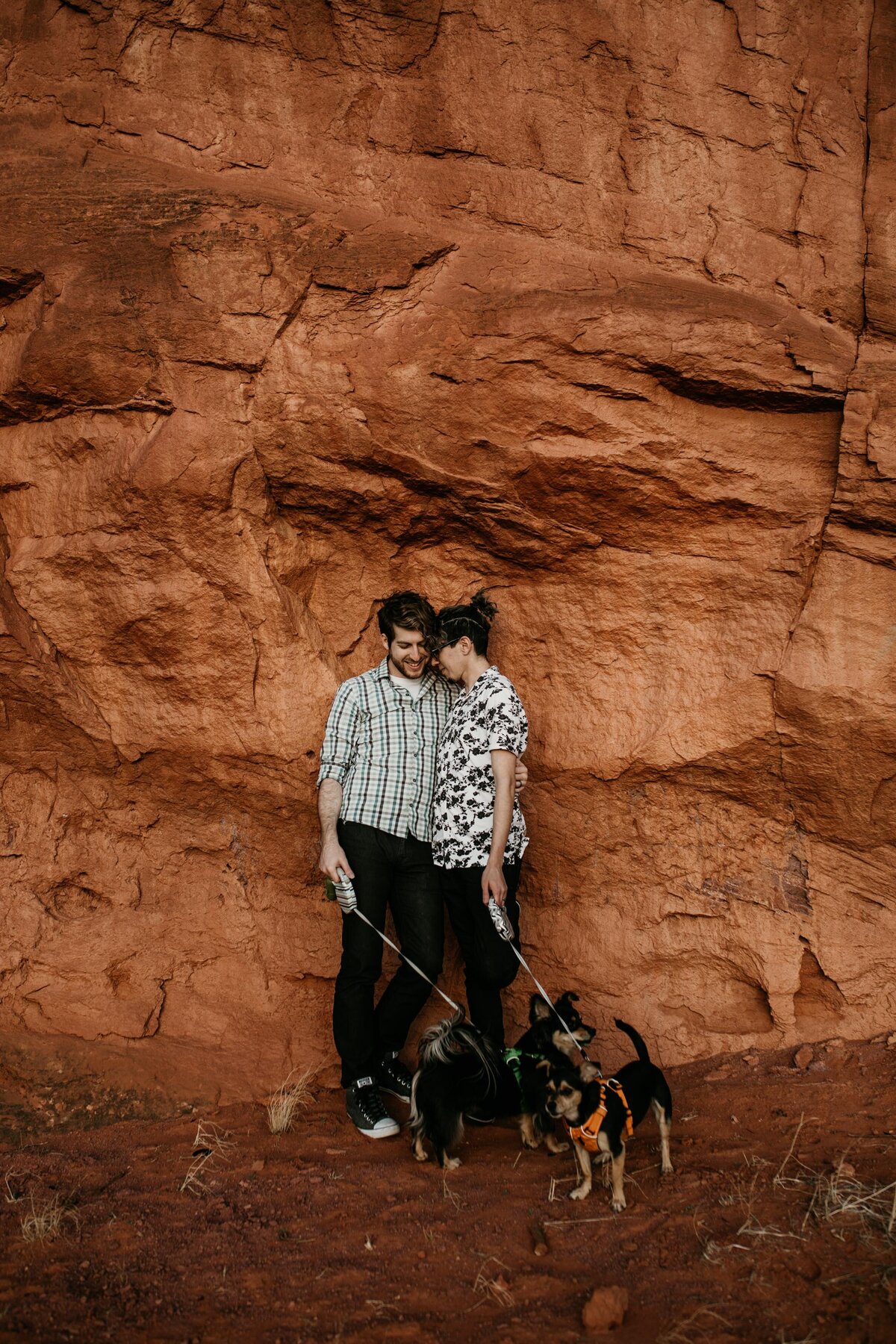 gay couple leaning against red rock with dogs