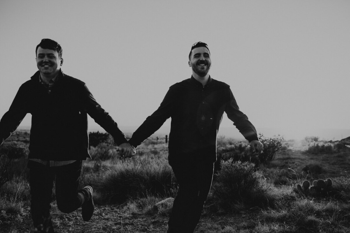 black and white two men holding hands and running