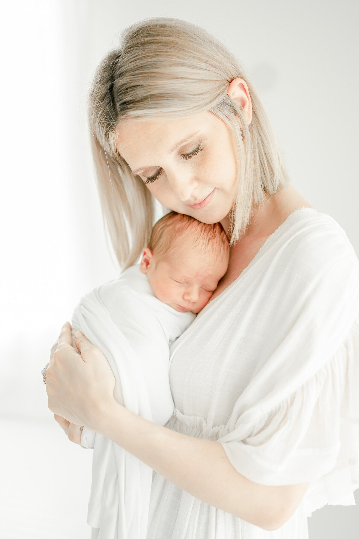 A mother in a white dress holds her baby Kristie Lloyd's Nashville newborn photographer studio