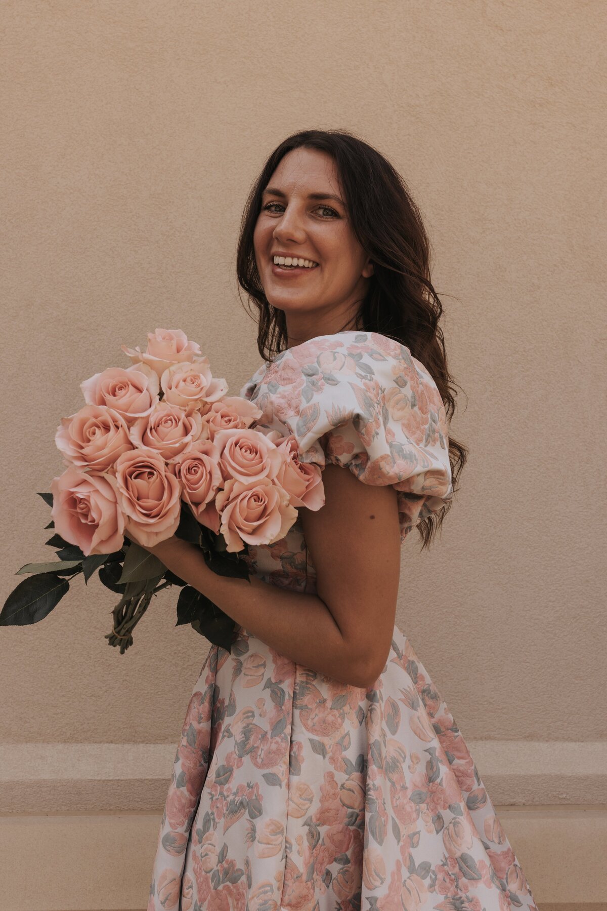 a woman in a pink floral dress holding a bouquet of pink roses