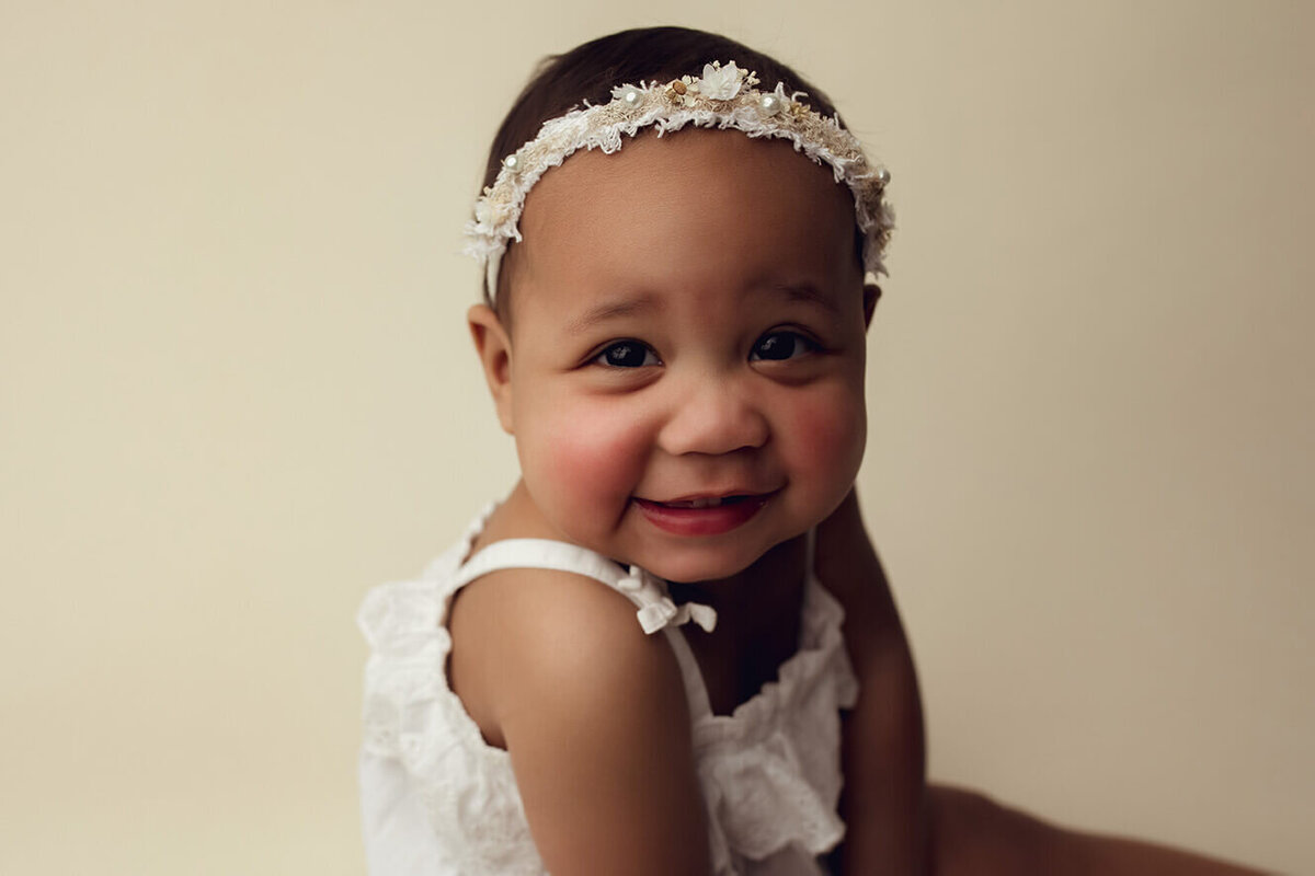a close up of a one year old girl smiling on a white backdrop