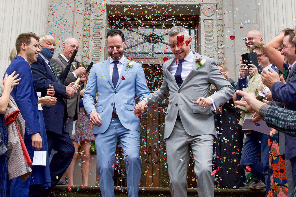 Groom and groom confetti exit at Marylebone Town Hall.  Holding hands
