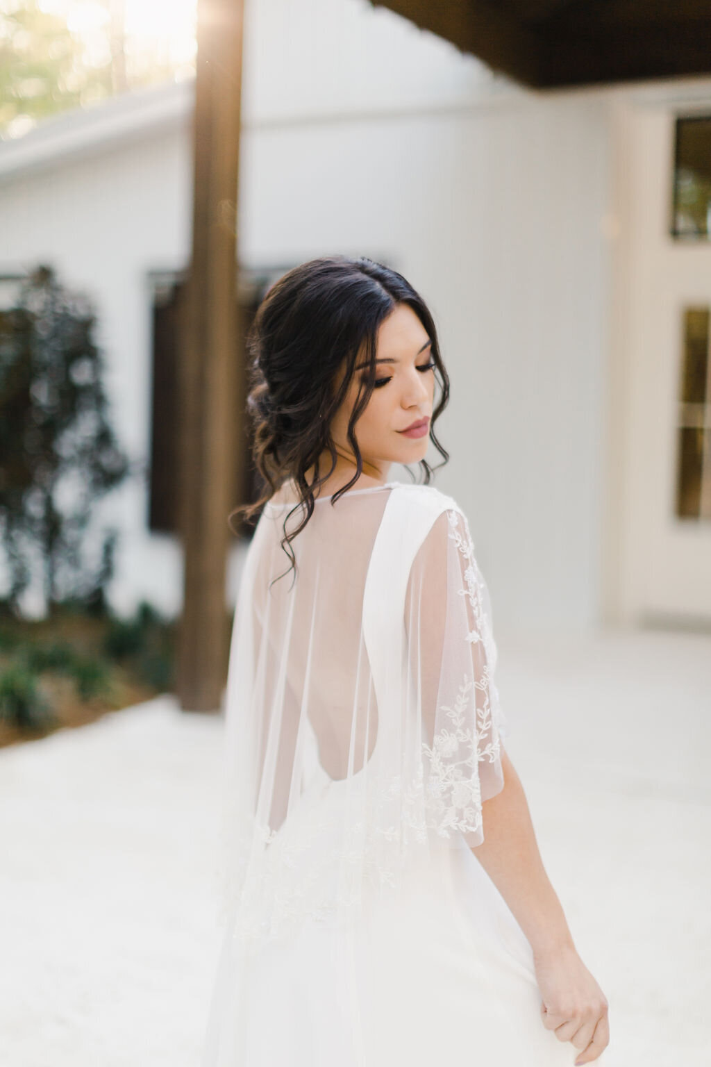 The beaded bridal capelet of the Dolores wedding dress style sits on the shoulders and is sheer to reveal the low scoop back.