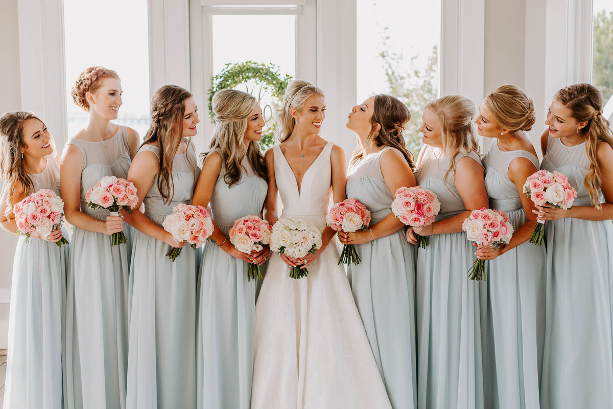 A bride is surrounded by her bridesmaids as they all smile at each other