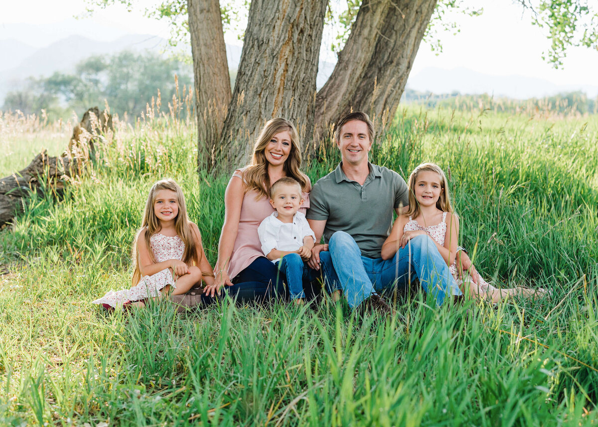 An attractive young family sits in a green field together underneath a big tree during their Northern Virginia family photo session