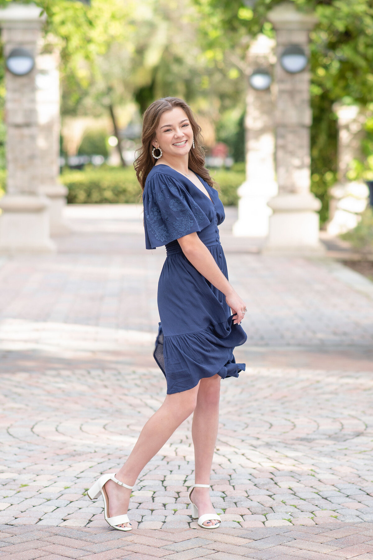 High school senior girl in blue dress twirling in brick walkway.