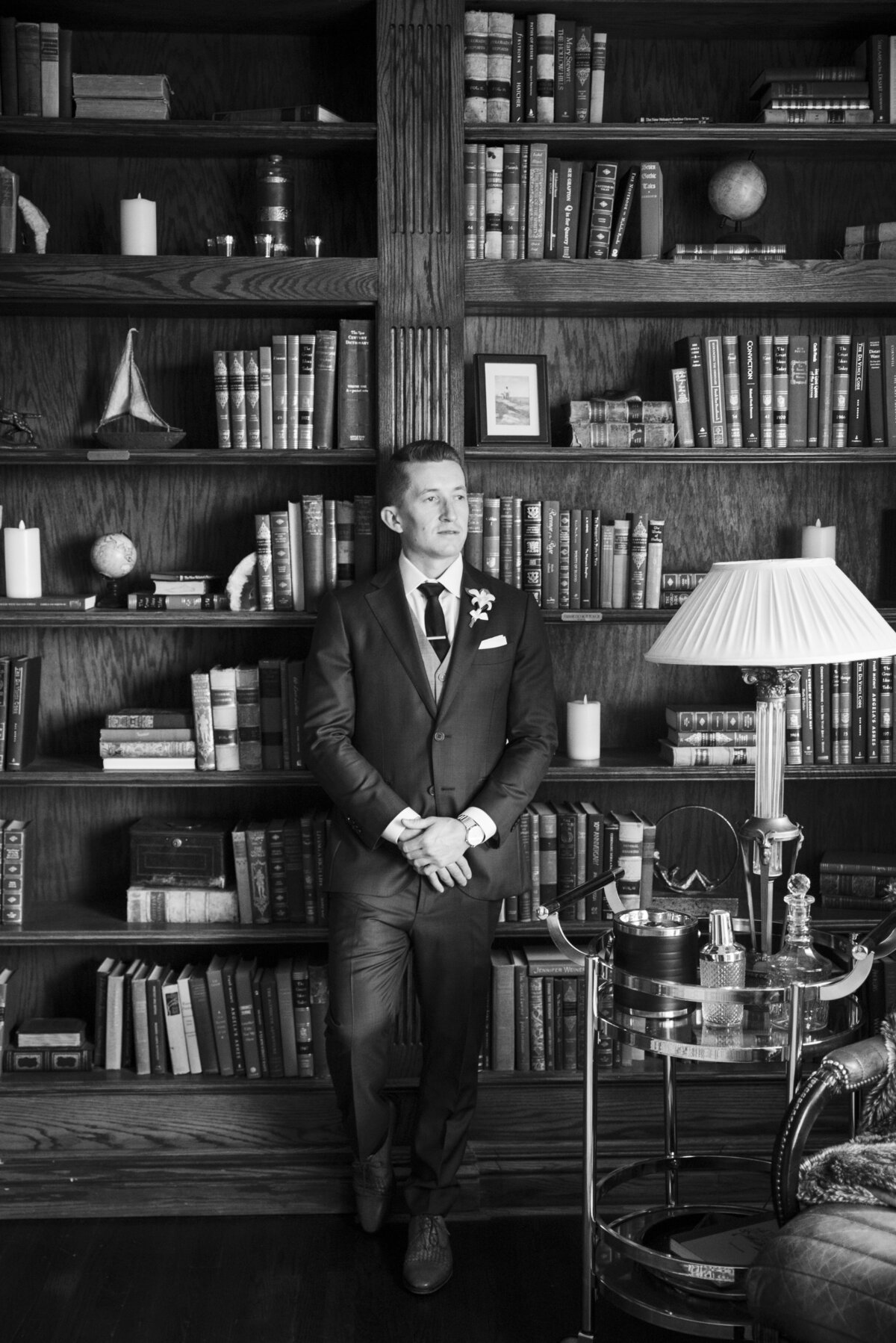 A groom leans against the bookcase in The Manor House library and looks into the distance.