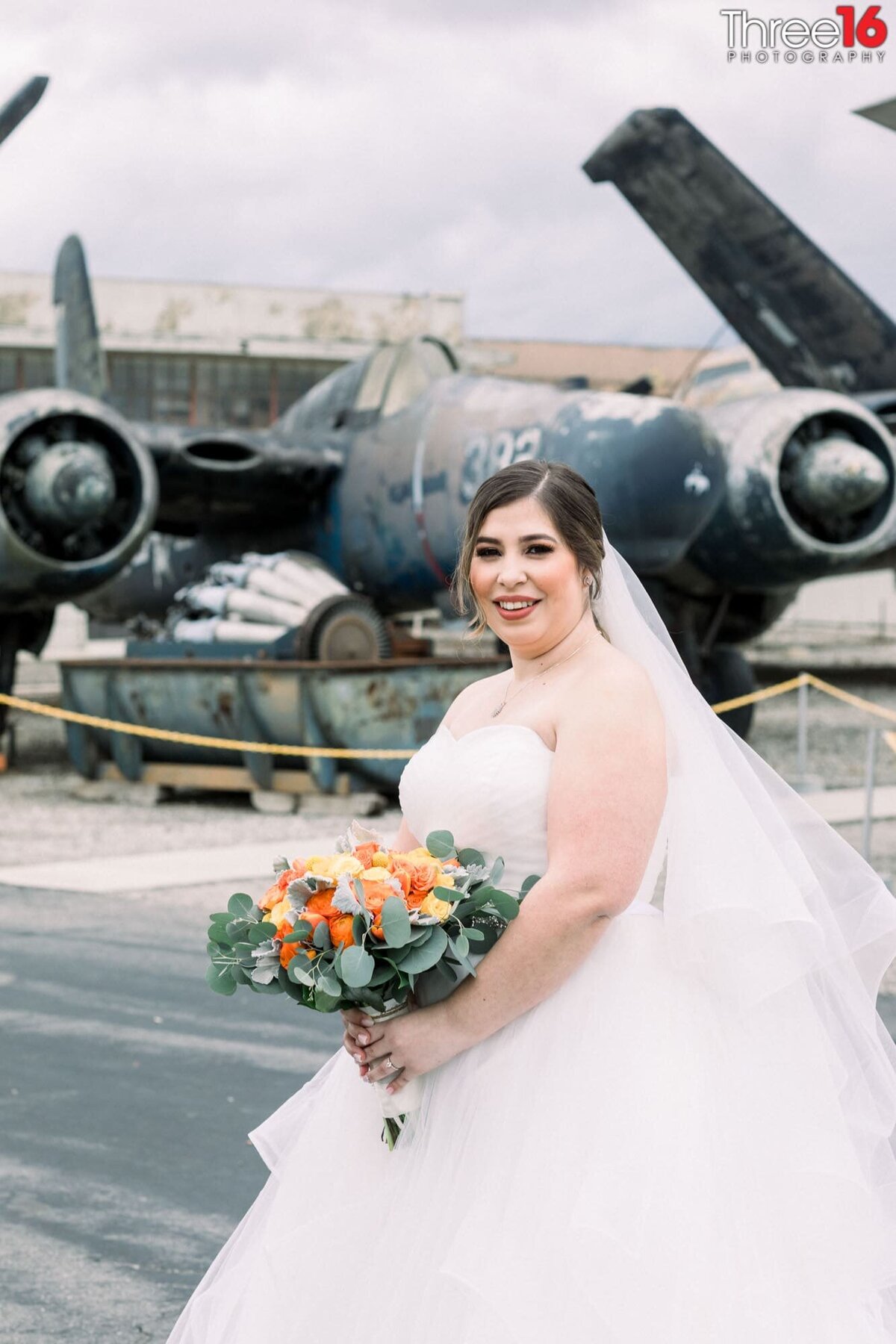 Bride poses with her bouquet with a classic plane in the background