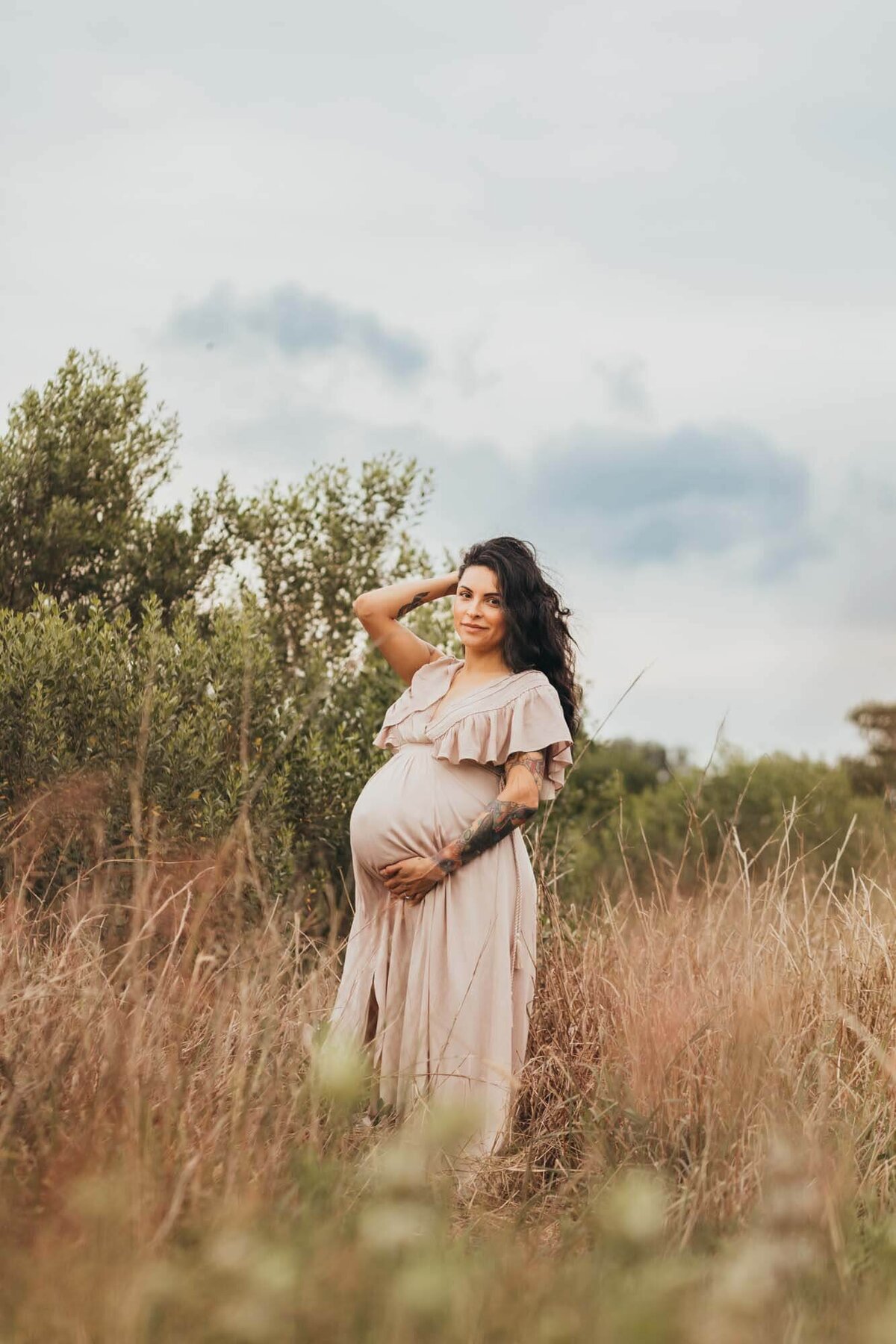 Maternity session of expectant mother holding her belly in a field wearing a Baltic Born dress in Houston.