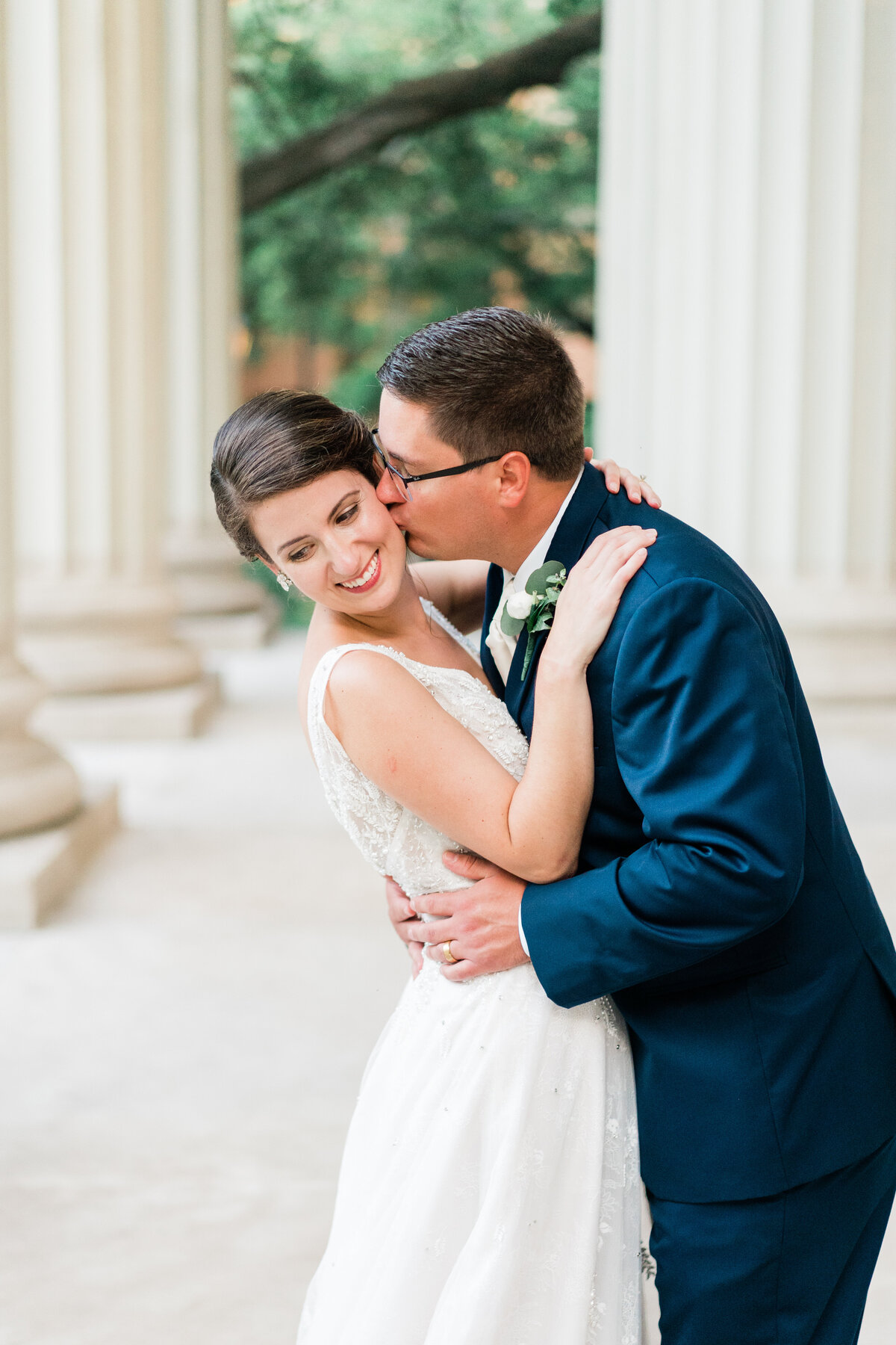 Groom kissing bride in front of columns