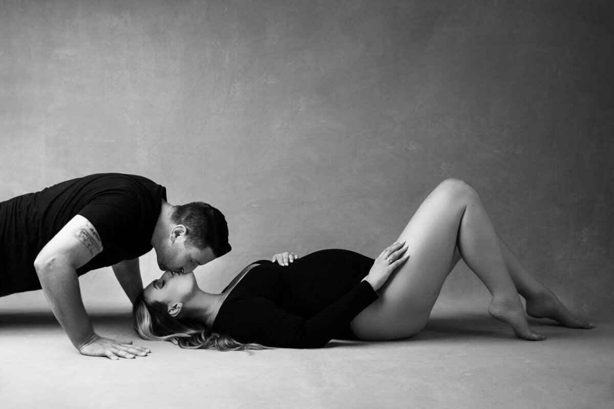 Pregnant mom laying on ground and kissing partner, taken by maternity photographer nj
