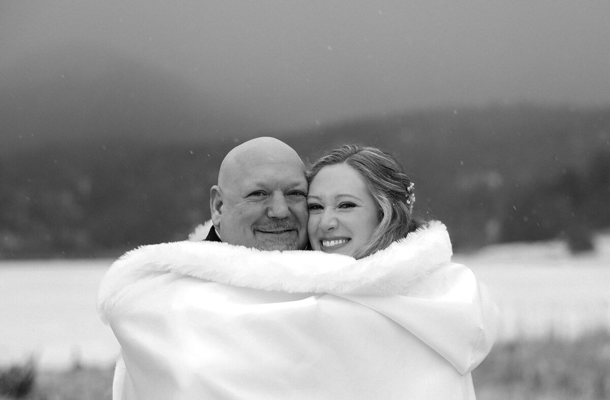 winter wedding in Colorado bride and groom snuggle under a blanket in the snow at Evergreen Lake House