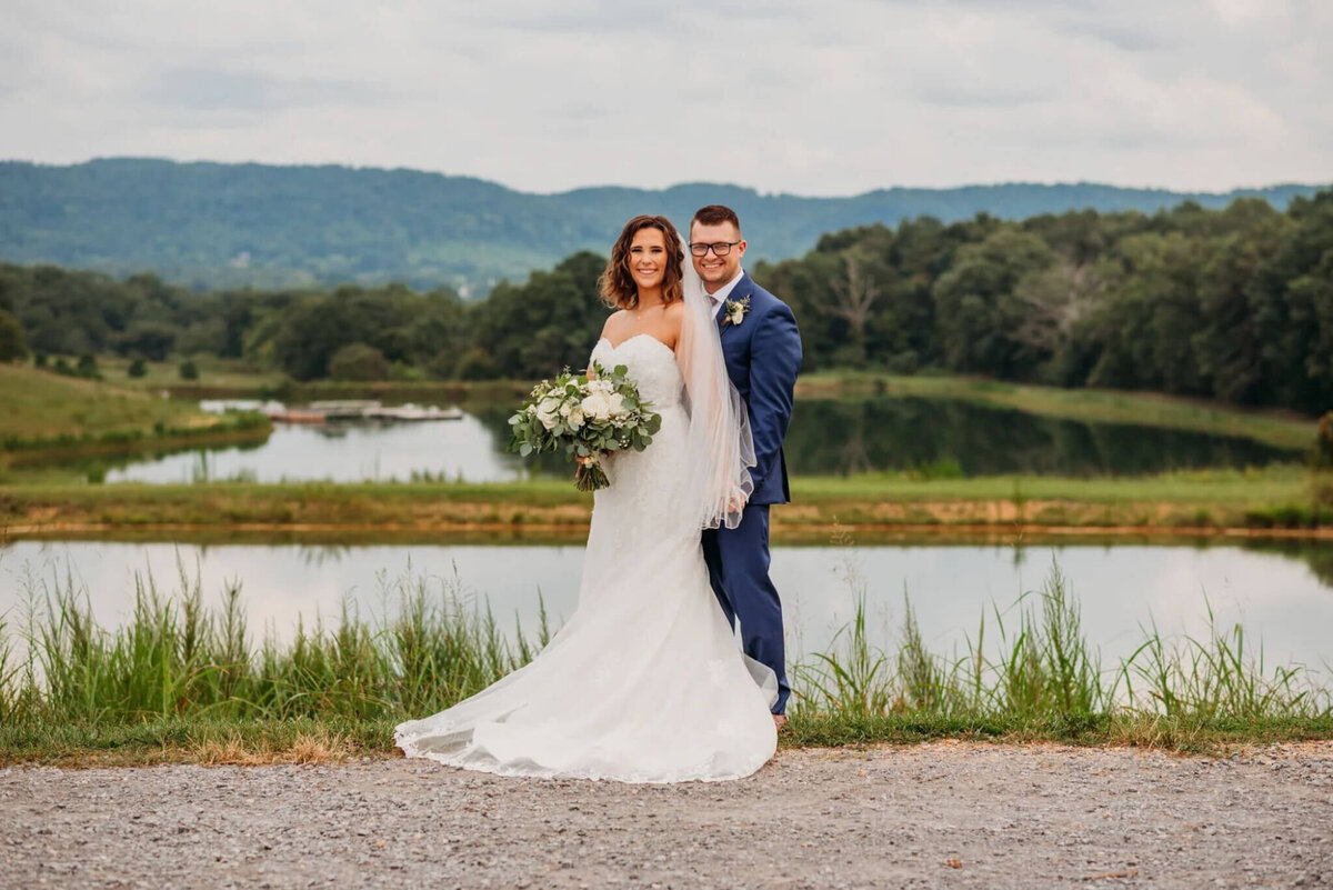 Photo of a groom standing behind his bride in front of a pond with Mountain View's