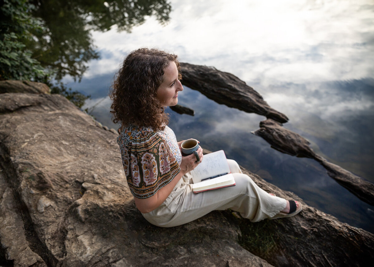 A solopreneur pensively looks out upon the water while sipping tea and writing in her journal during her personal branding session with Ingrid Berrios Photography.