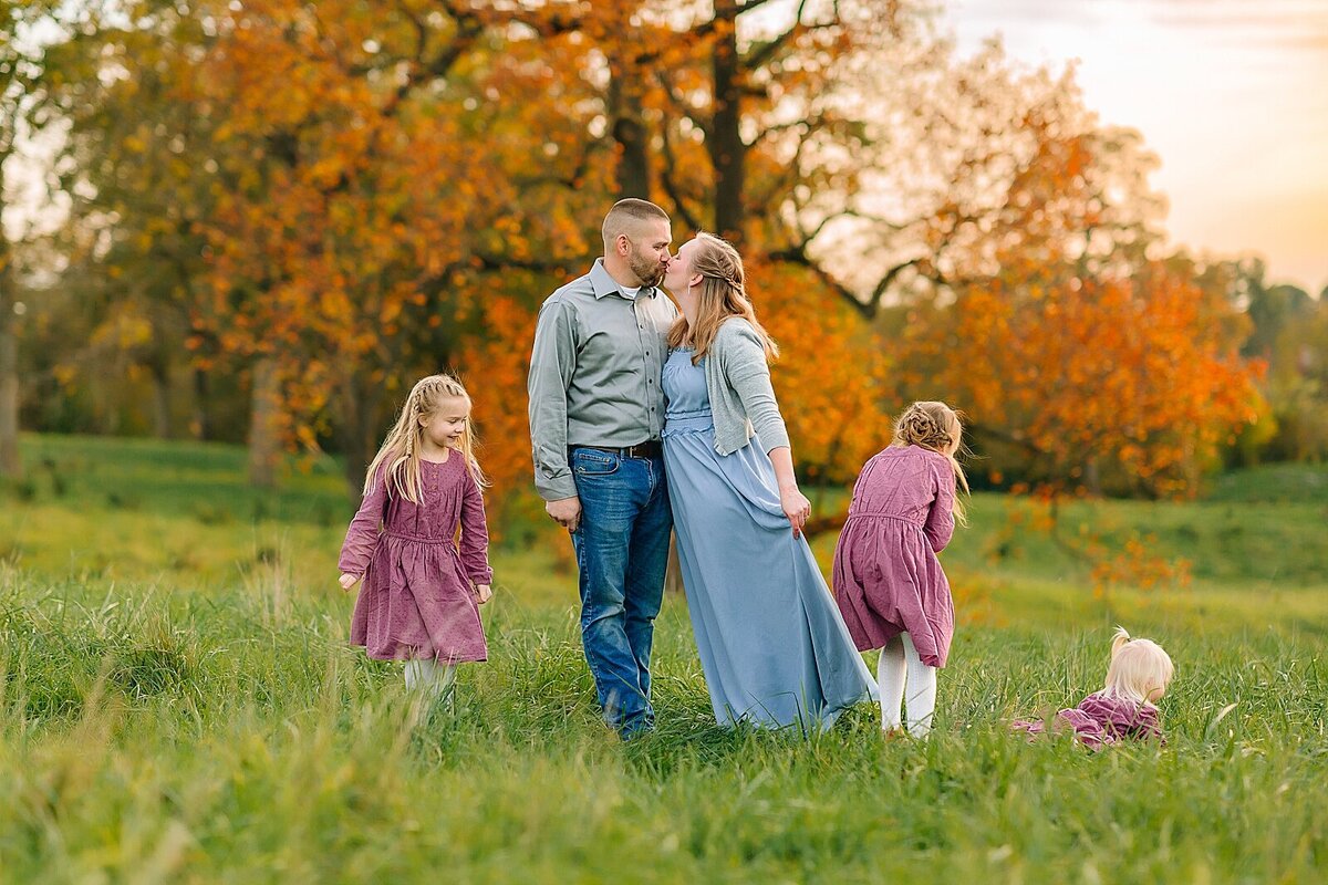 Mom and dad kissing in a field while children play