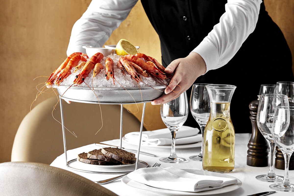 Waiter placing seafood platter of prawns on ice on the table.
