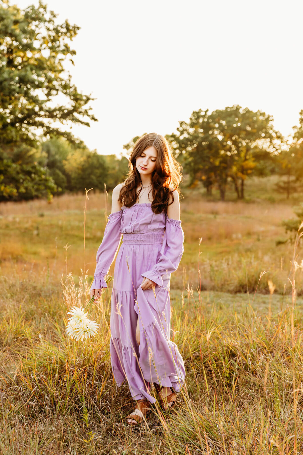 brown haired teen girl playing with long purple dress & holding flowers for senior photography session