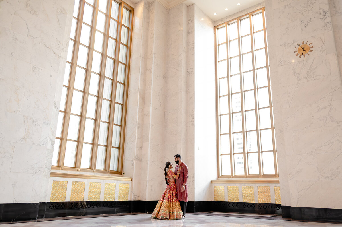 Indian couple look at each other in front of large windows at Old Post Office Chicago, IL