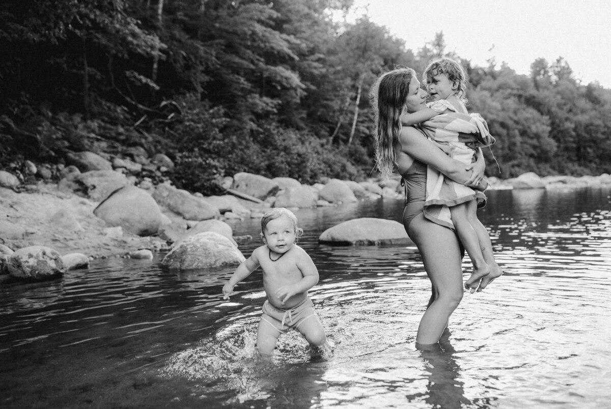 Mother holding child in river with other child running nearby in Austin, Texas