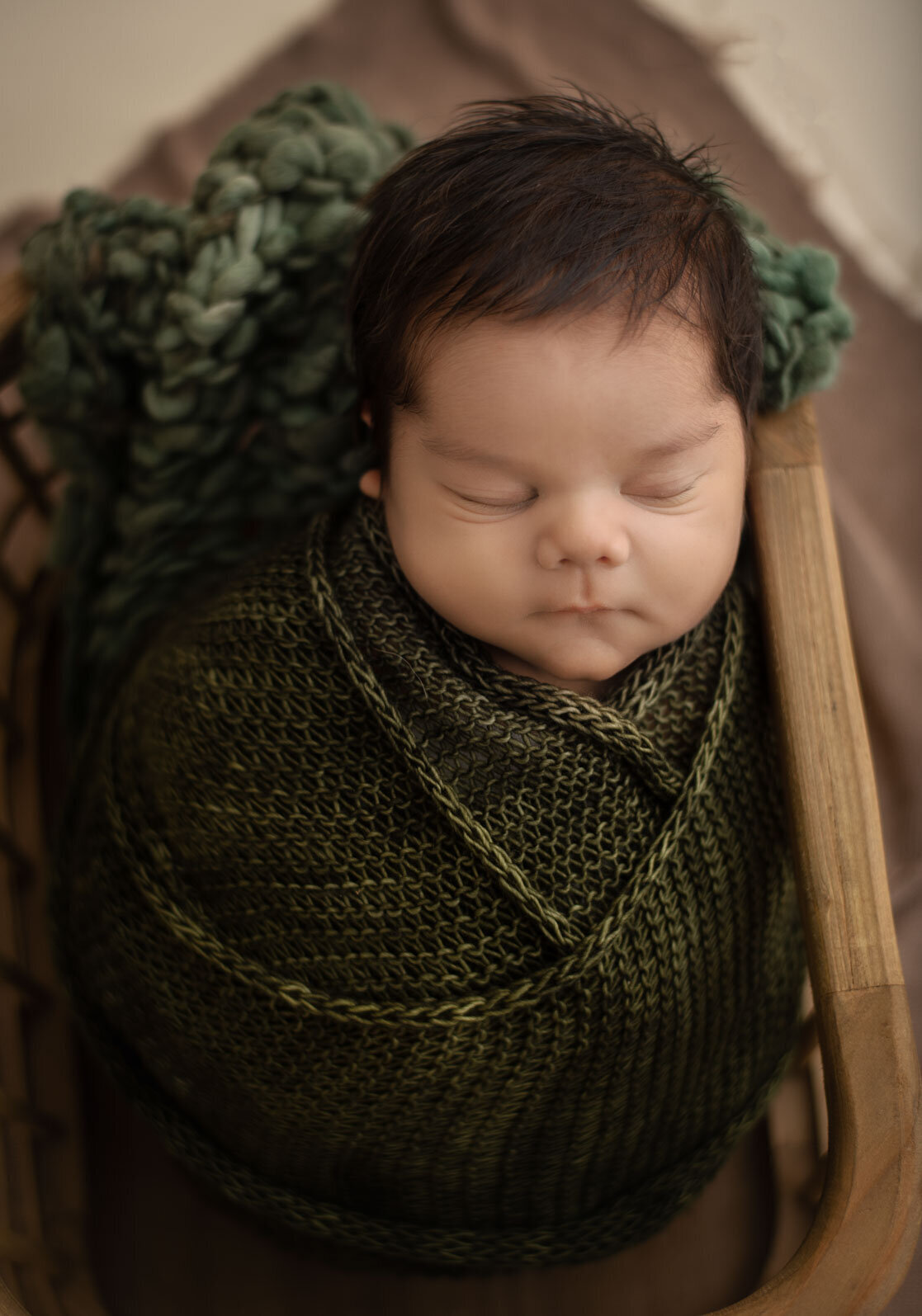 baby wrapped in green with green blanket under head in a newborn basket prop