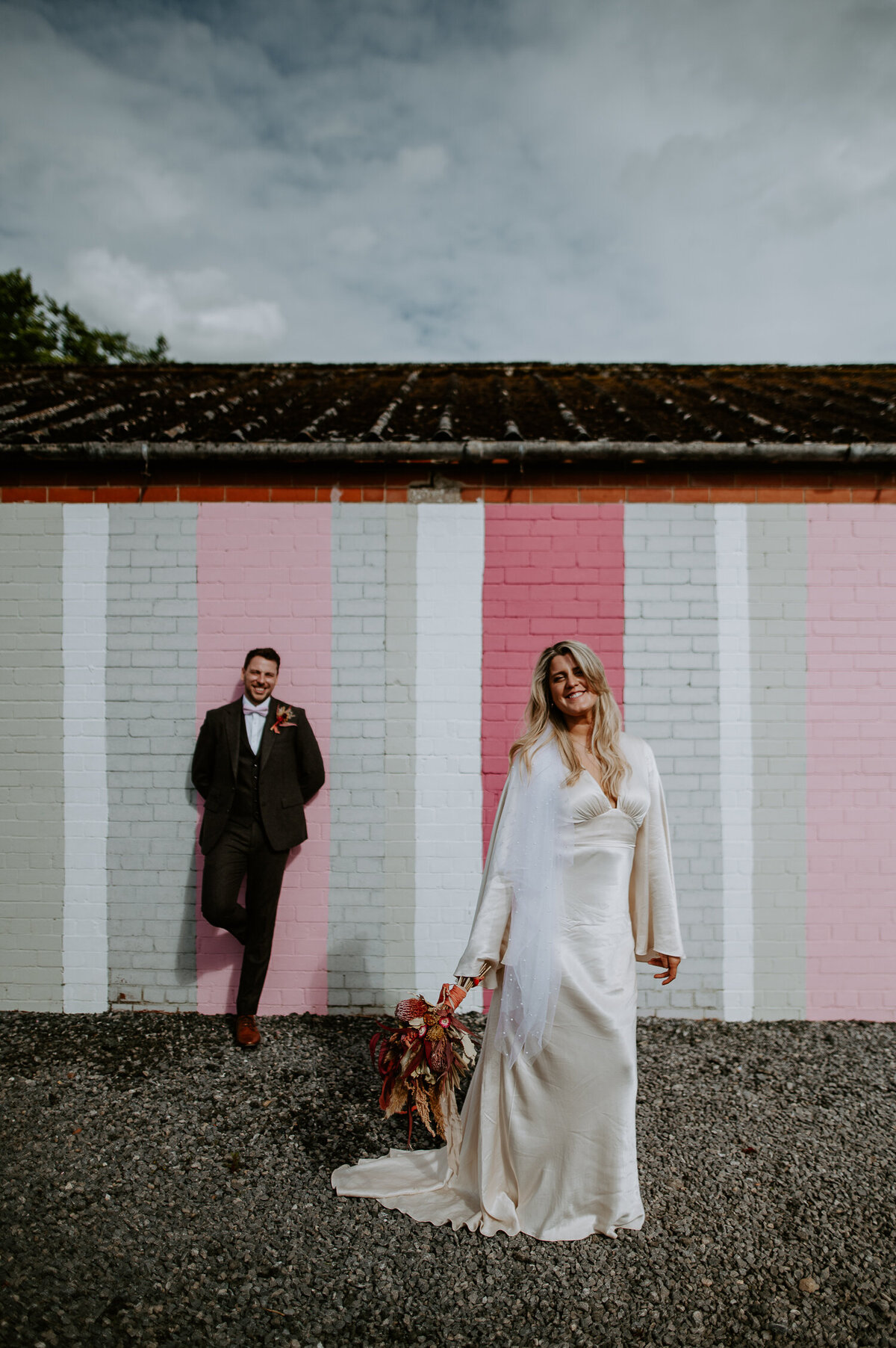 A Bride and Groom stand infant of a pink mural wall at White Syke Fields, a barn wedding venue in york with great natural light.