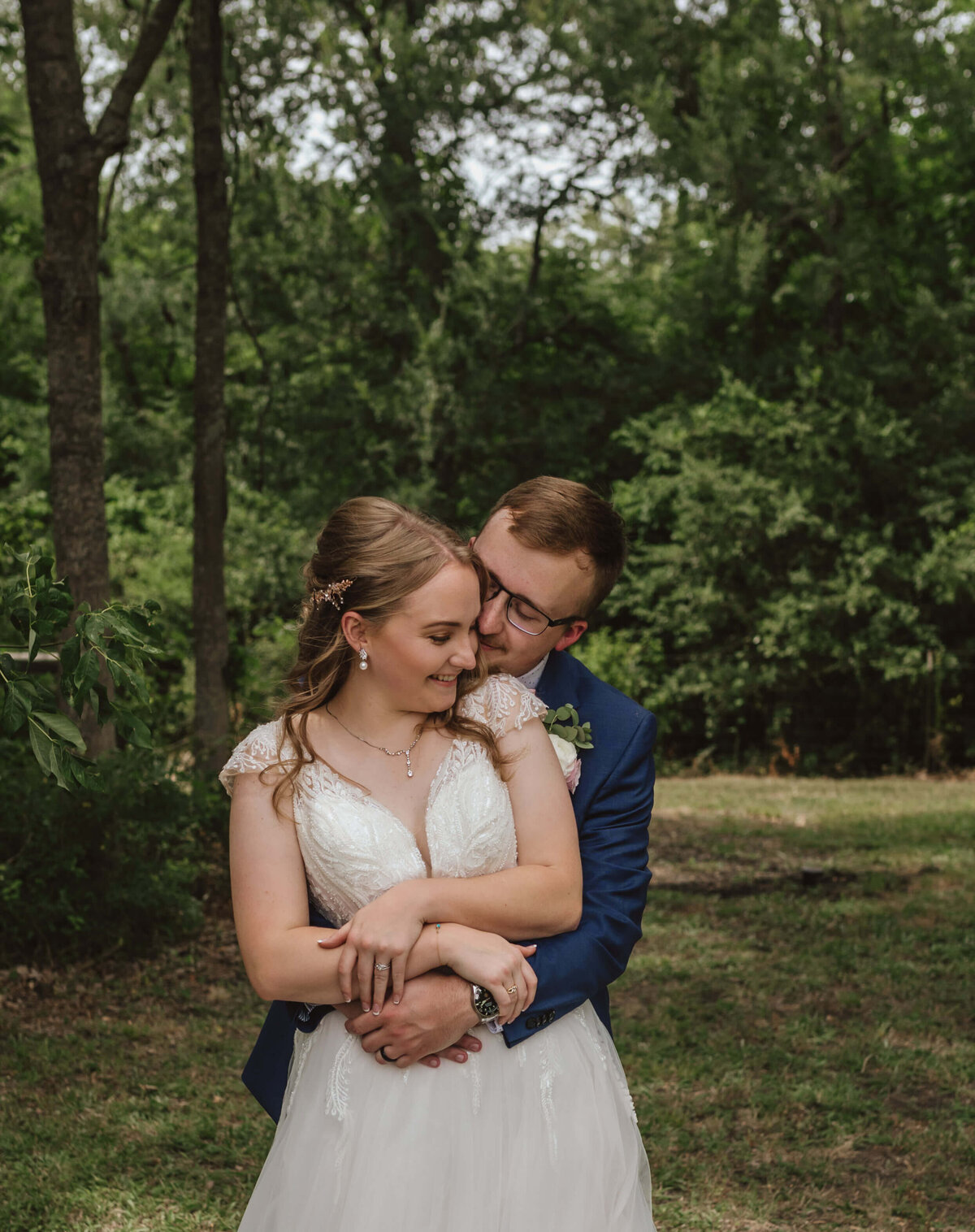 groom hugs bride tightly outside surrounded by greenery after intimate wedding ceremony