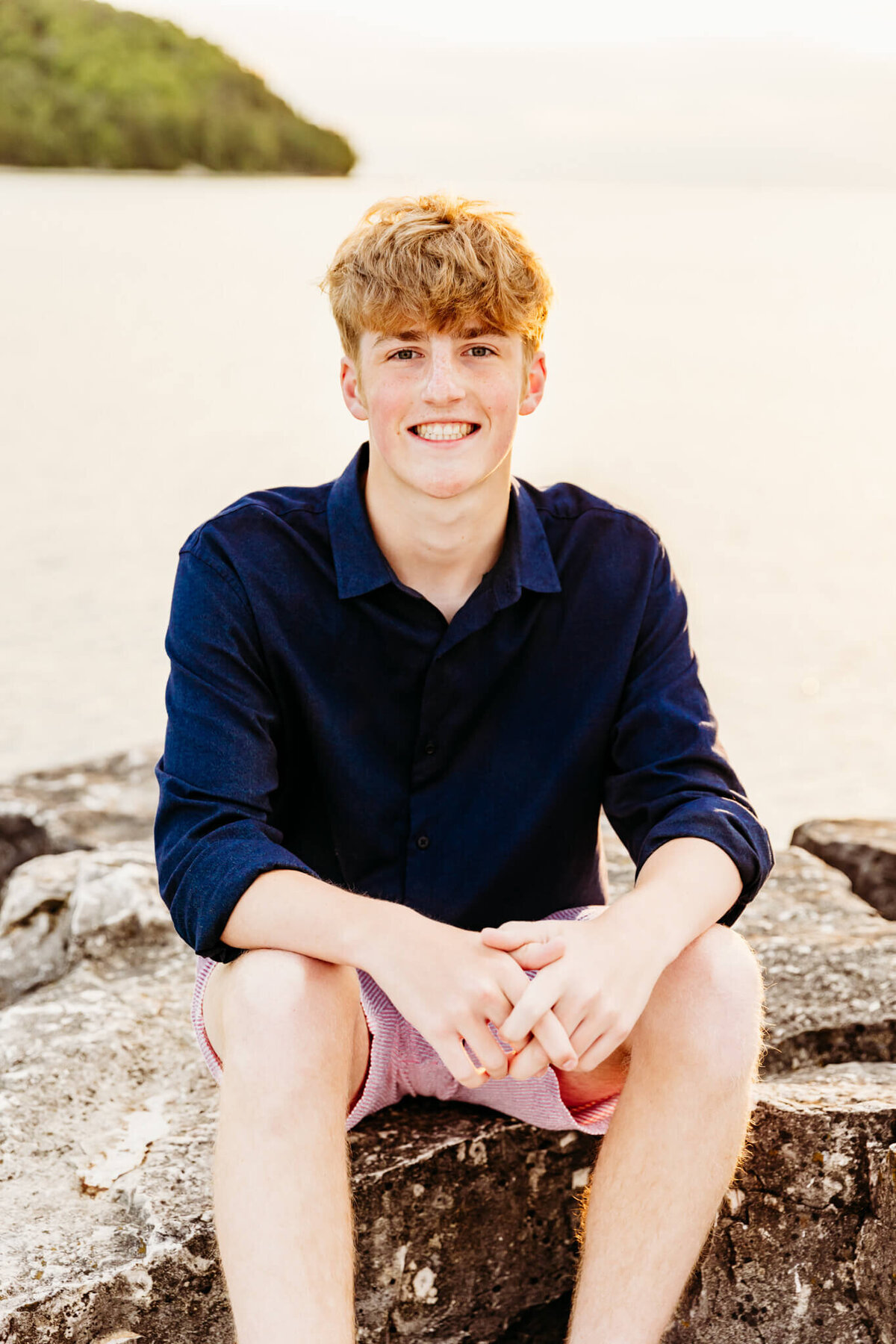 young man sitting on rocks at Sister Bay marina during senior photo session