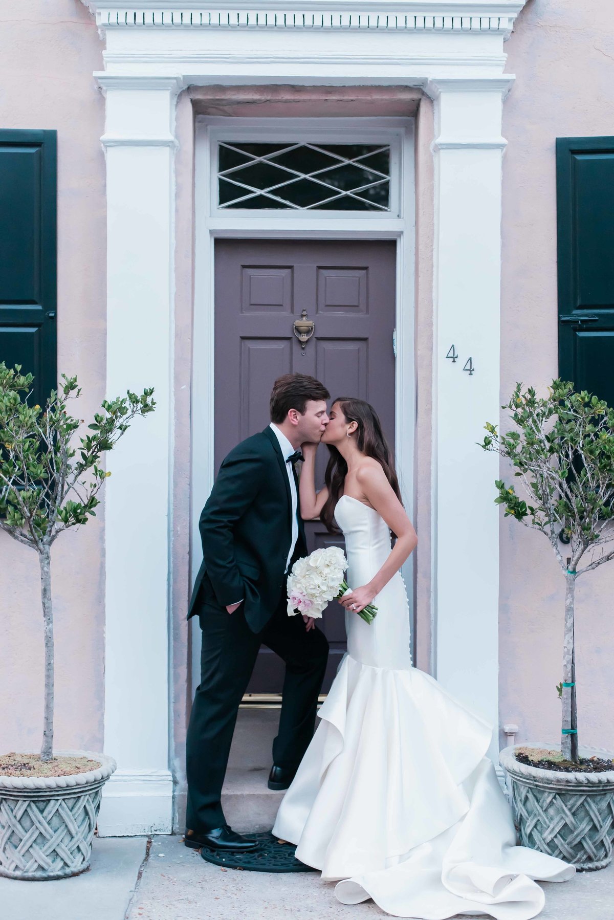 Bride and groom kiss in a traditional pink doorway in Charleston, SC