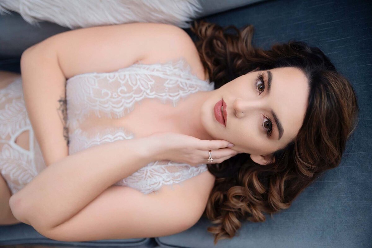 Brunette woman in white lace bodysuit posing on  blue couch