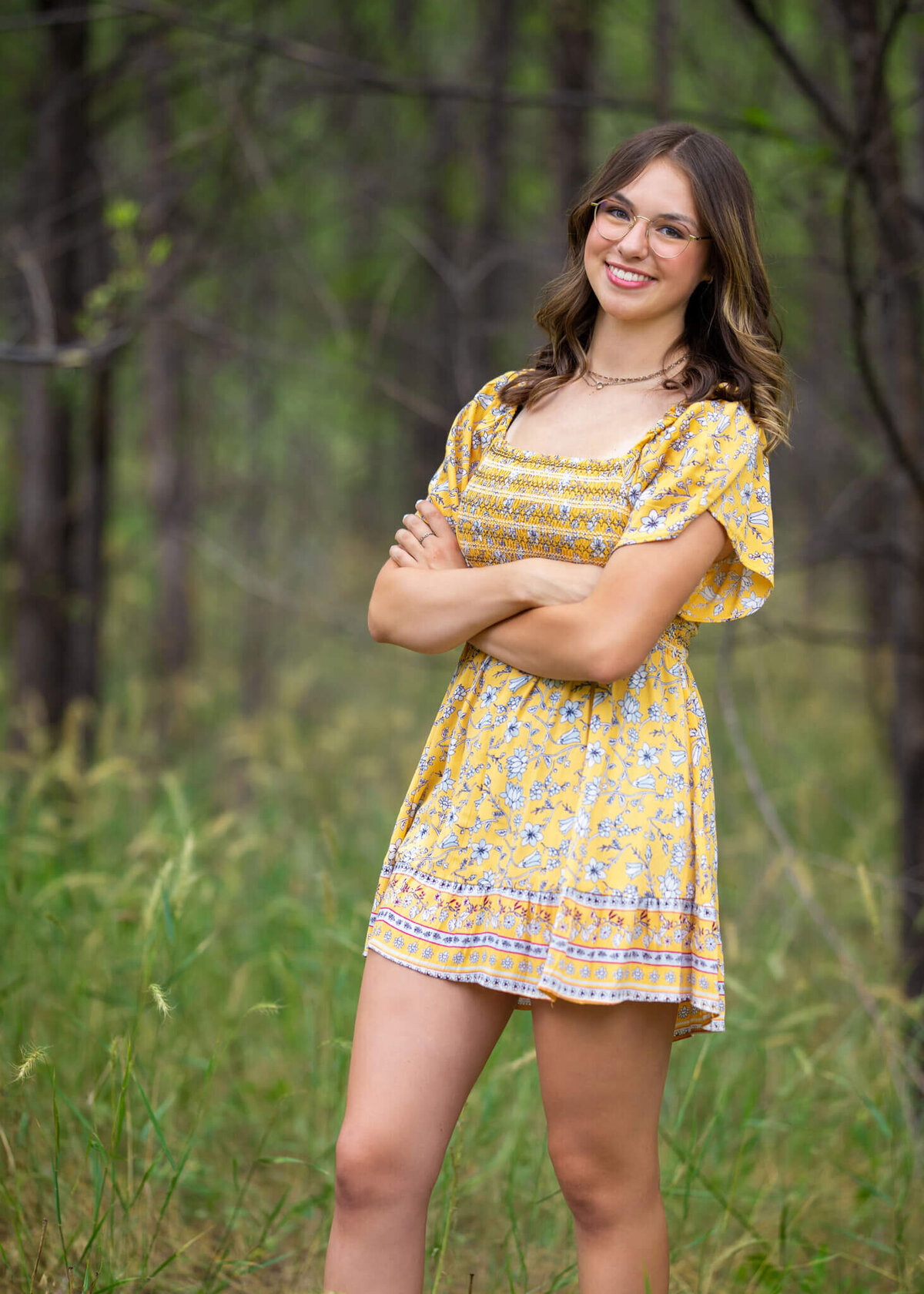 high school senior girl in a yellow sun dress standing in a  forest