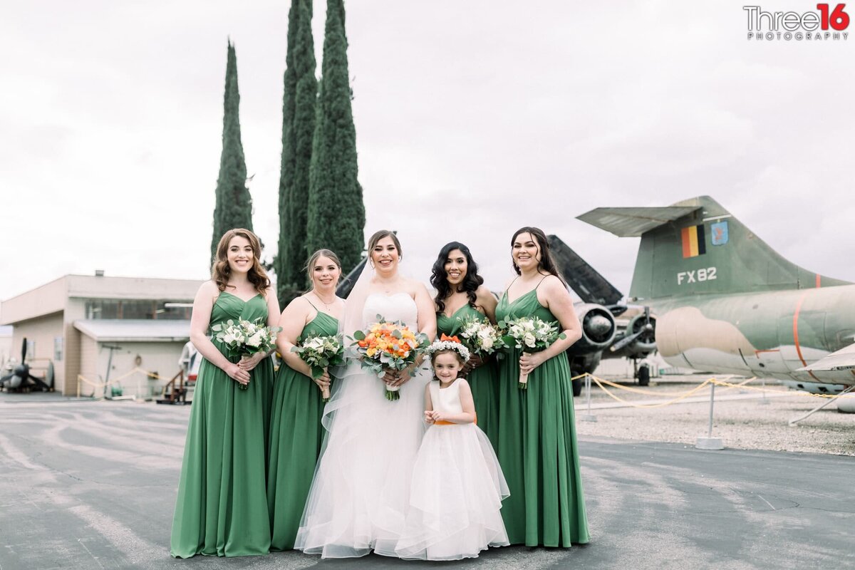 Bride poses with her Bridesmaids and Flower Girl before the ceremony at the Planes of Fame Museum