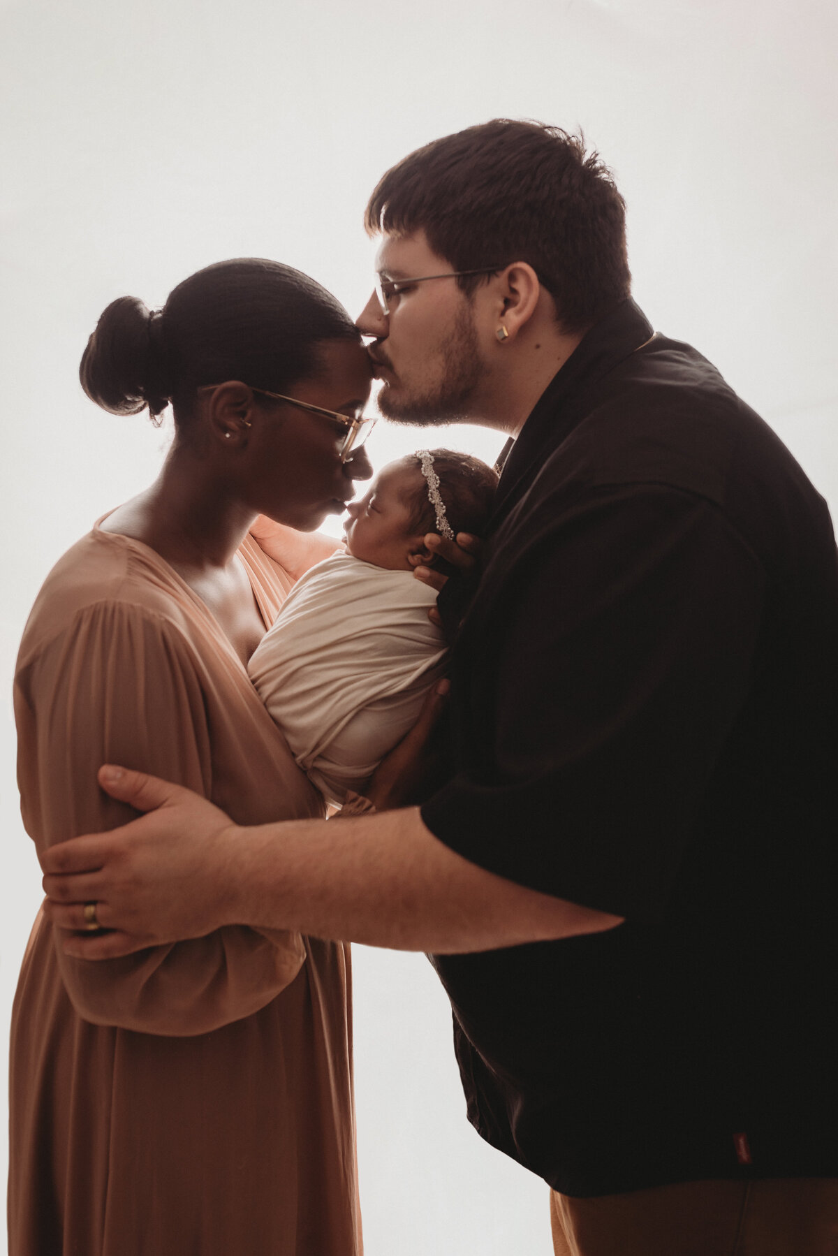Newborn family portrait of dad kissing mom's forehead and mom kissing baby's nose at Marietta, GA newborn photography studio with mom, dad and baby girl wearing blush pink, cream and black